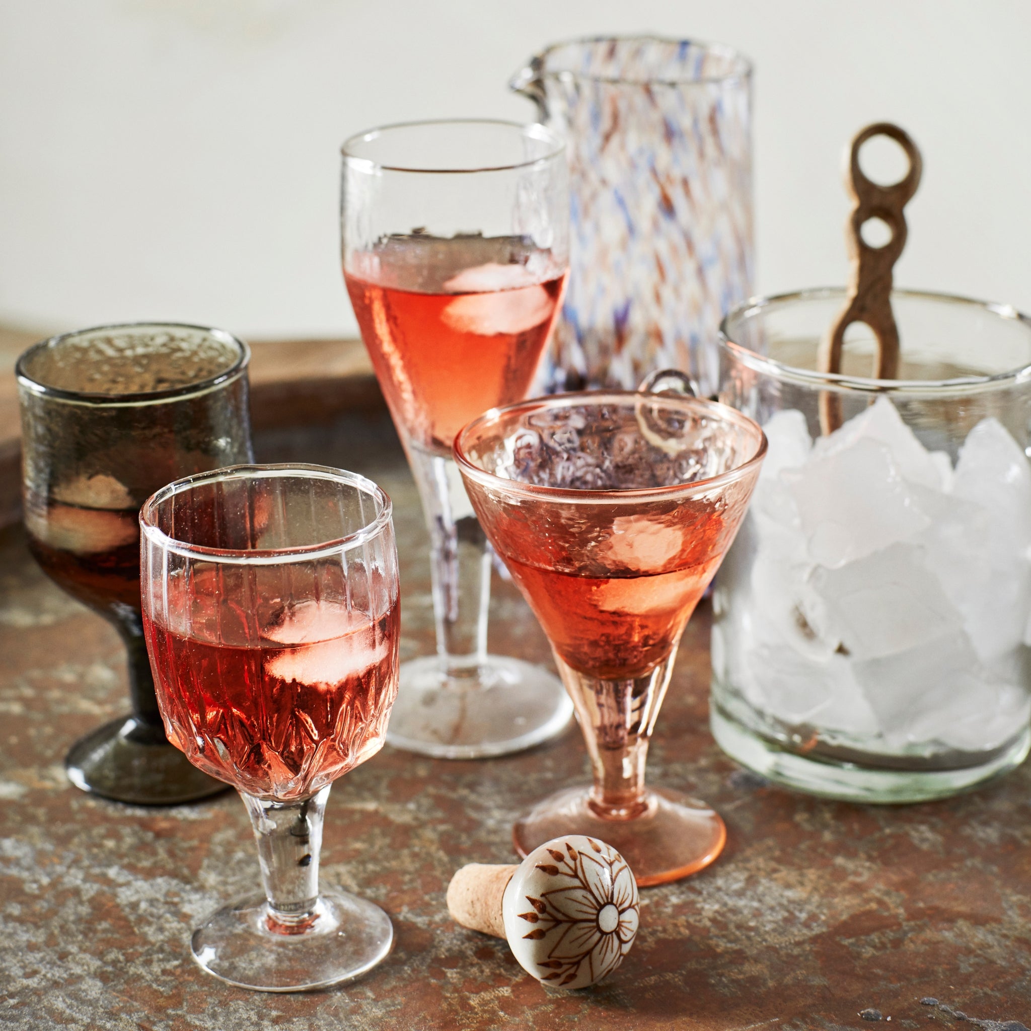 Decoratieve flessen voorzien van handgemaakte flessenstoppers, gecombineerd met kleurrijke glazen, perfect voor het serveren van wijn of andere dranken tijdens een stijlvolle borrel.
