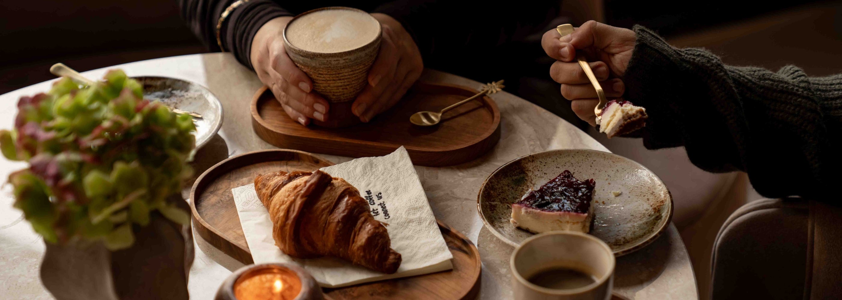 Gezellige café-at-home setting met koffie, croissants en porseleinen mokken – een warm moment van rust en samenzijn aan tafel.
