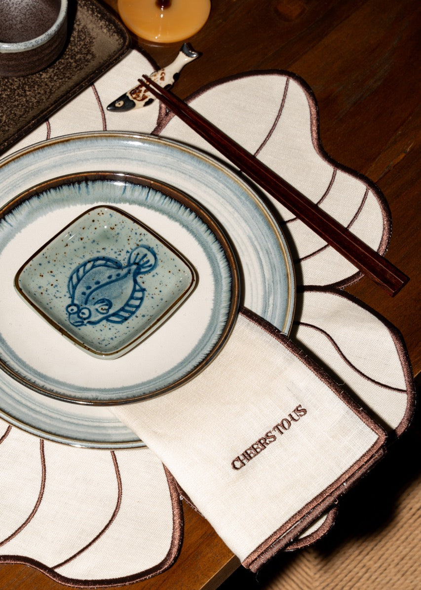 Close-up van de Seaside Stories tafelsetting met porseleinen borden, kleine schaaltjes en houten details in een rustige, warme sfeer.