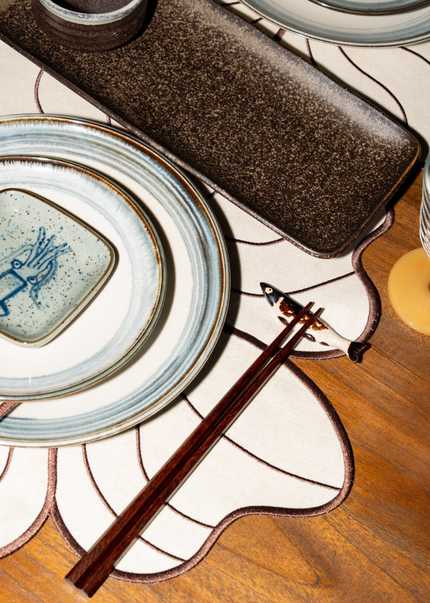 Detailfoto van servies en tafeldecoratie in aardse tinten en subtiele zeeblauwe accenten, passend bij de Seaside Stories sfeer.