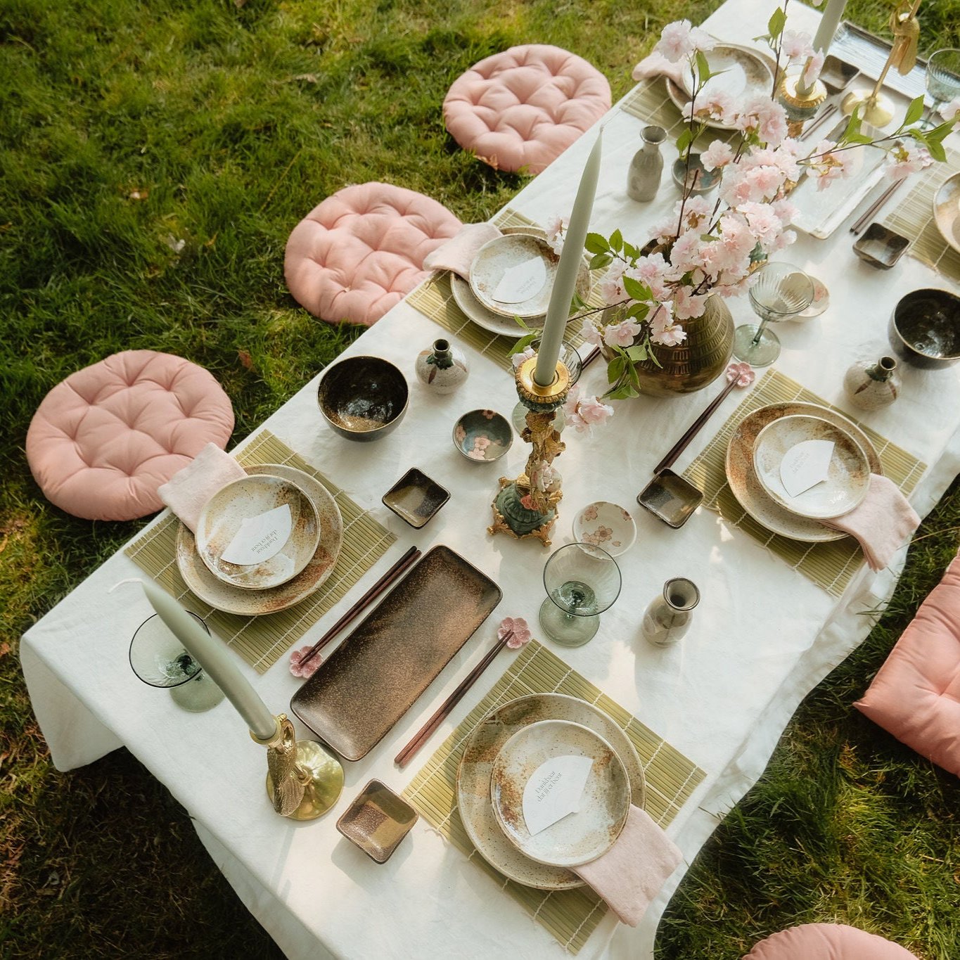 Elegant gedekte eettafel in de tuin met bloemen, aardewerken servies, en roze zitkussens.