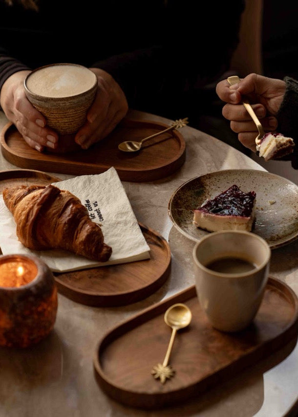 Intiem koffiemoment aan tafel met latte, espresso, brownie en vers gebak, gestyled met gouden bestek en natuurlijke materialen uit de Café at Home collectie.