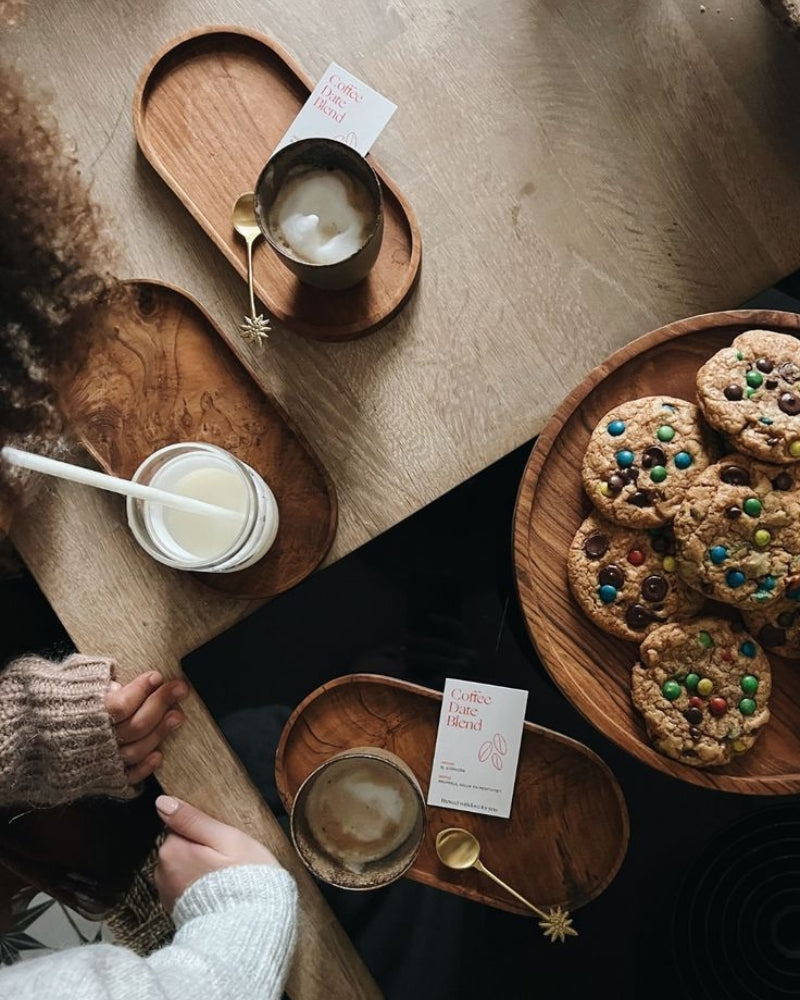 Bovenaanzicht van een knus cafémoment thuis met koffie, gebak en warme details.