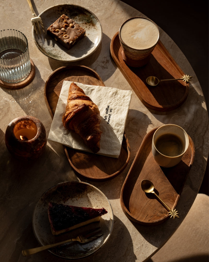Intiem koffiemoment aan tafel met latte, espresso, brownie en vers gebak, gestyled met gouden bestek en natuurlijke materialen uit de Café at Home collectie.