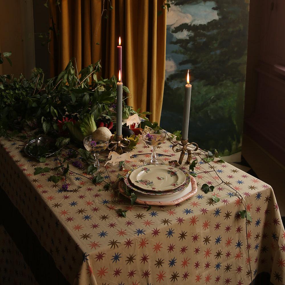 Gezellige kersttafel gedekt met het Noa Sterren Tafelkleed van Doing Goods, met kleurrijke sterren en warme beige tint voor een sfeervolle setting.