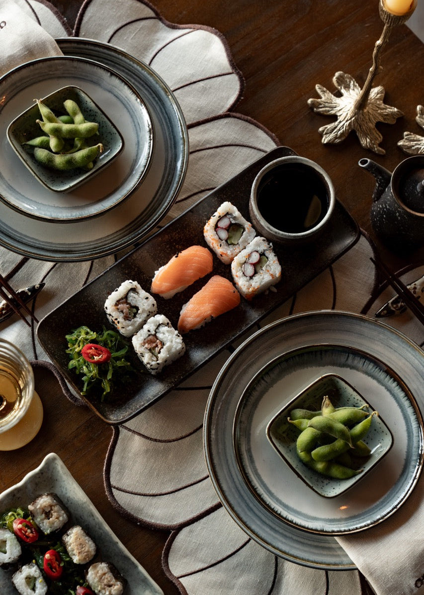 Overzichtsfoto van een gedekte tafel met keramiek, hout en linnen in een kalm kleurpalet van beige, bruin en lichtblauw.