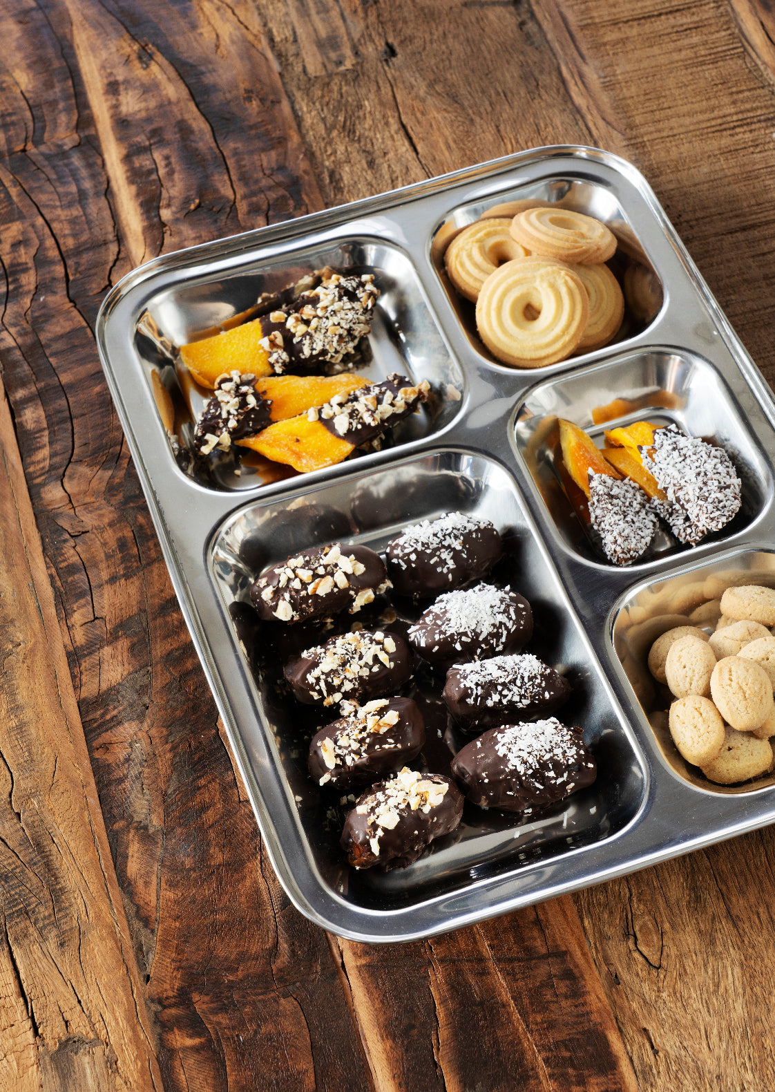 Stainless steel food tray gevuld met snacks op een minimalistische tafelsetting.